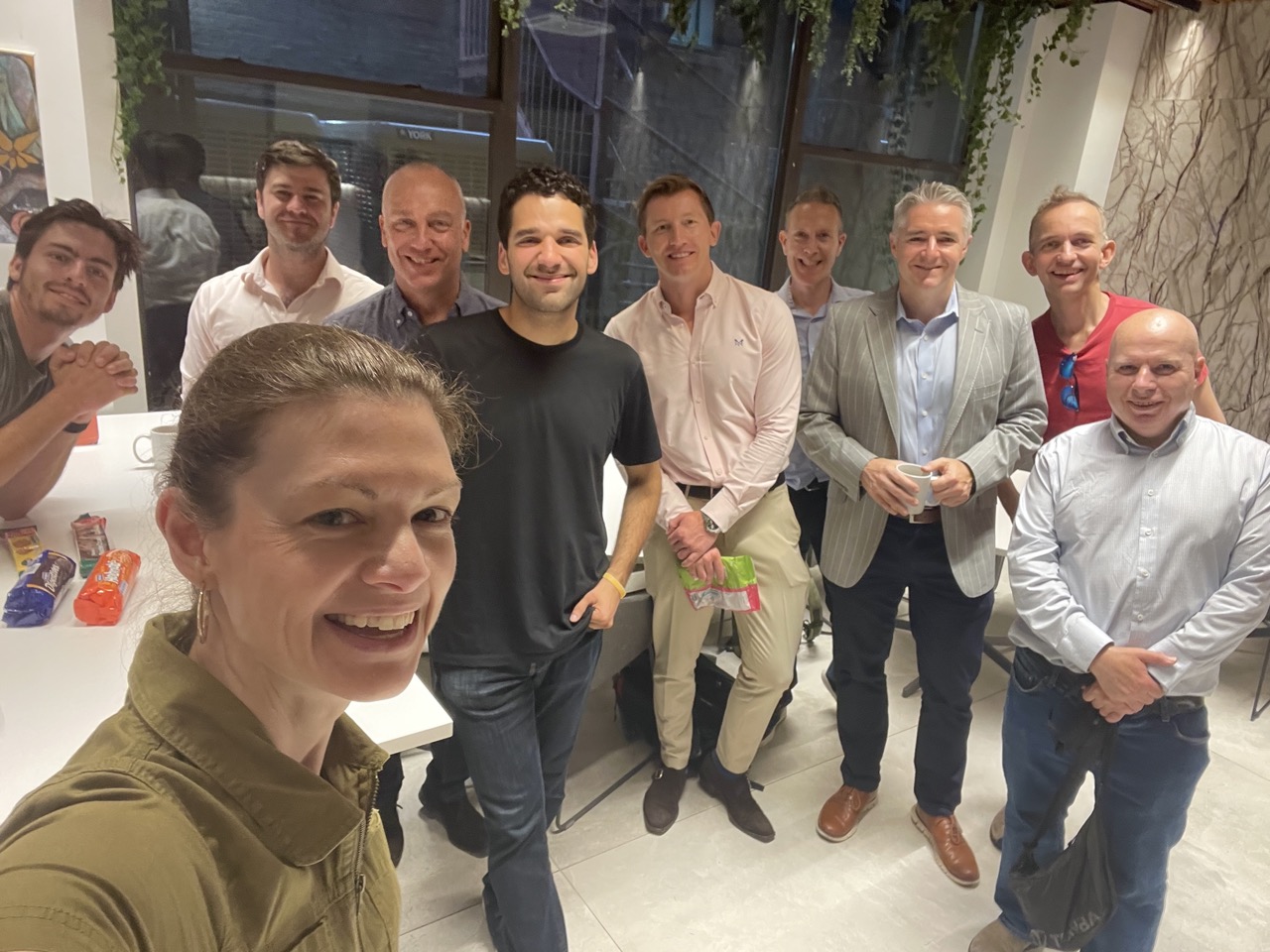 Smiling woman takes a group selfie with nine men in an office