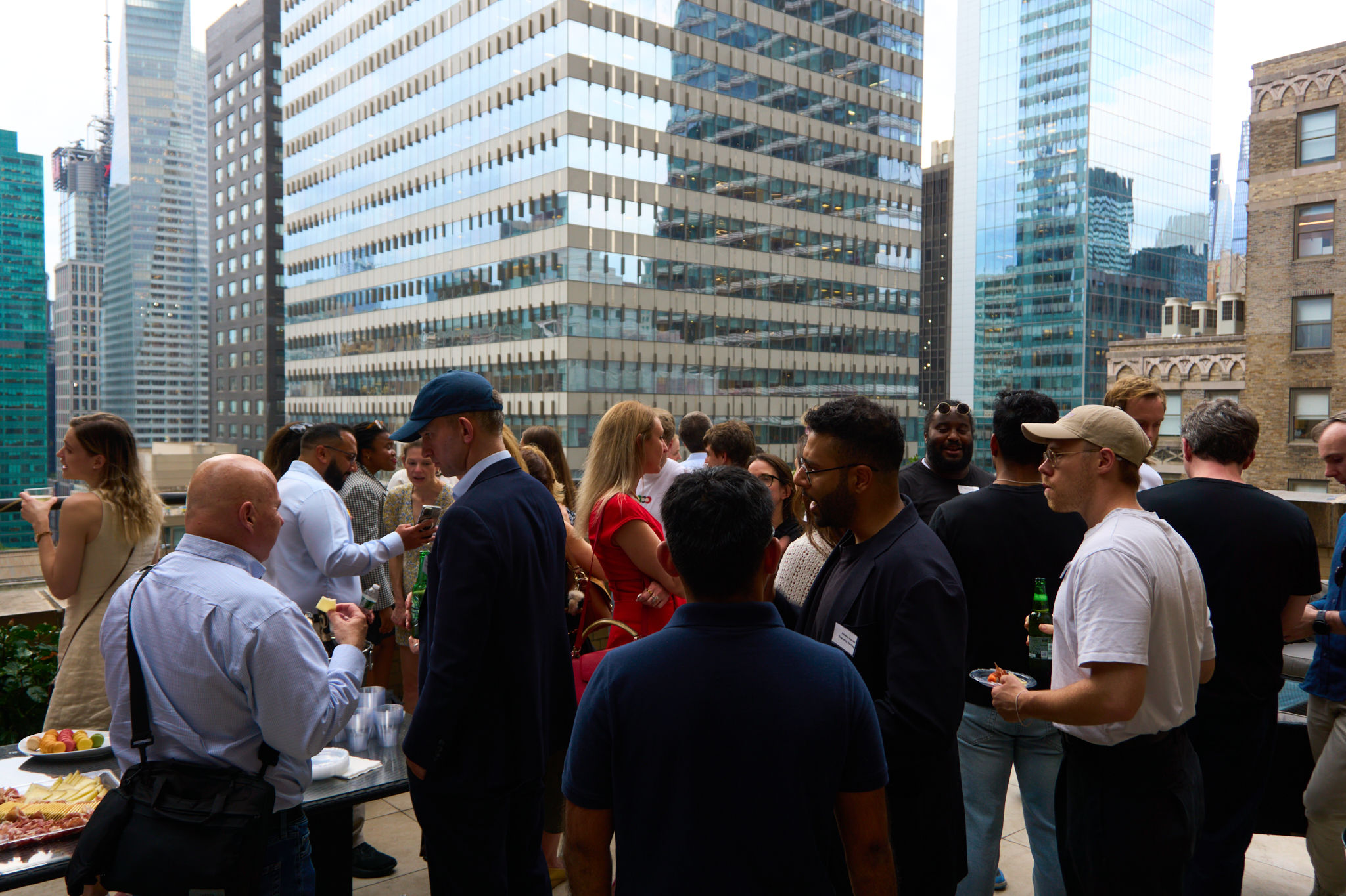 People mingle at a rooftop gathering surrounded by city skyscrapers