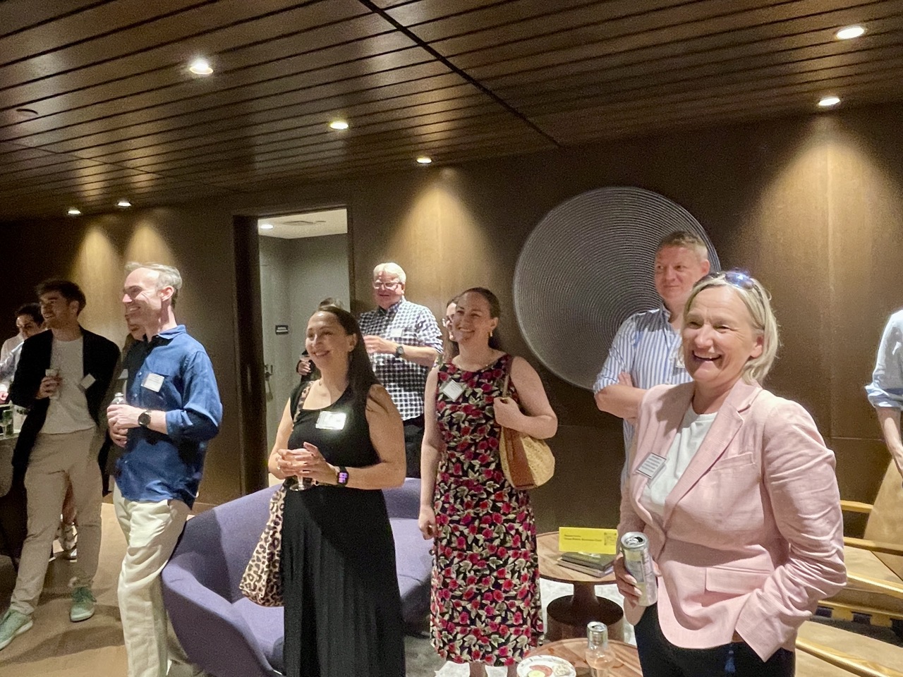 Smiling adults wearing name badges mingle with drinks in a lounge.